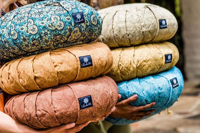 a pair of hands holding colourful yoga cushions